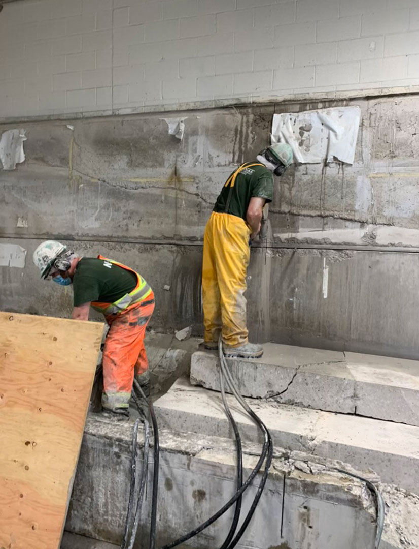 workers cutting through concrete wall and floor using hand saws